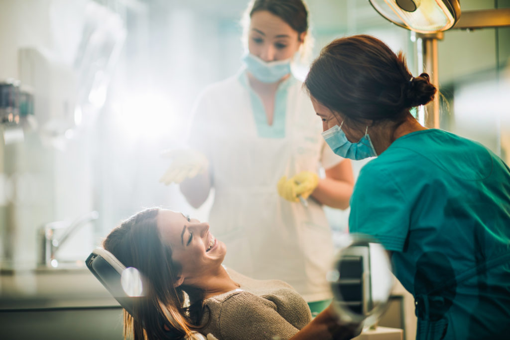 Smiling woman sitting in dentist chair and talking to her dentist before teeth examination.